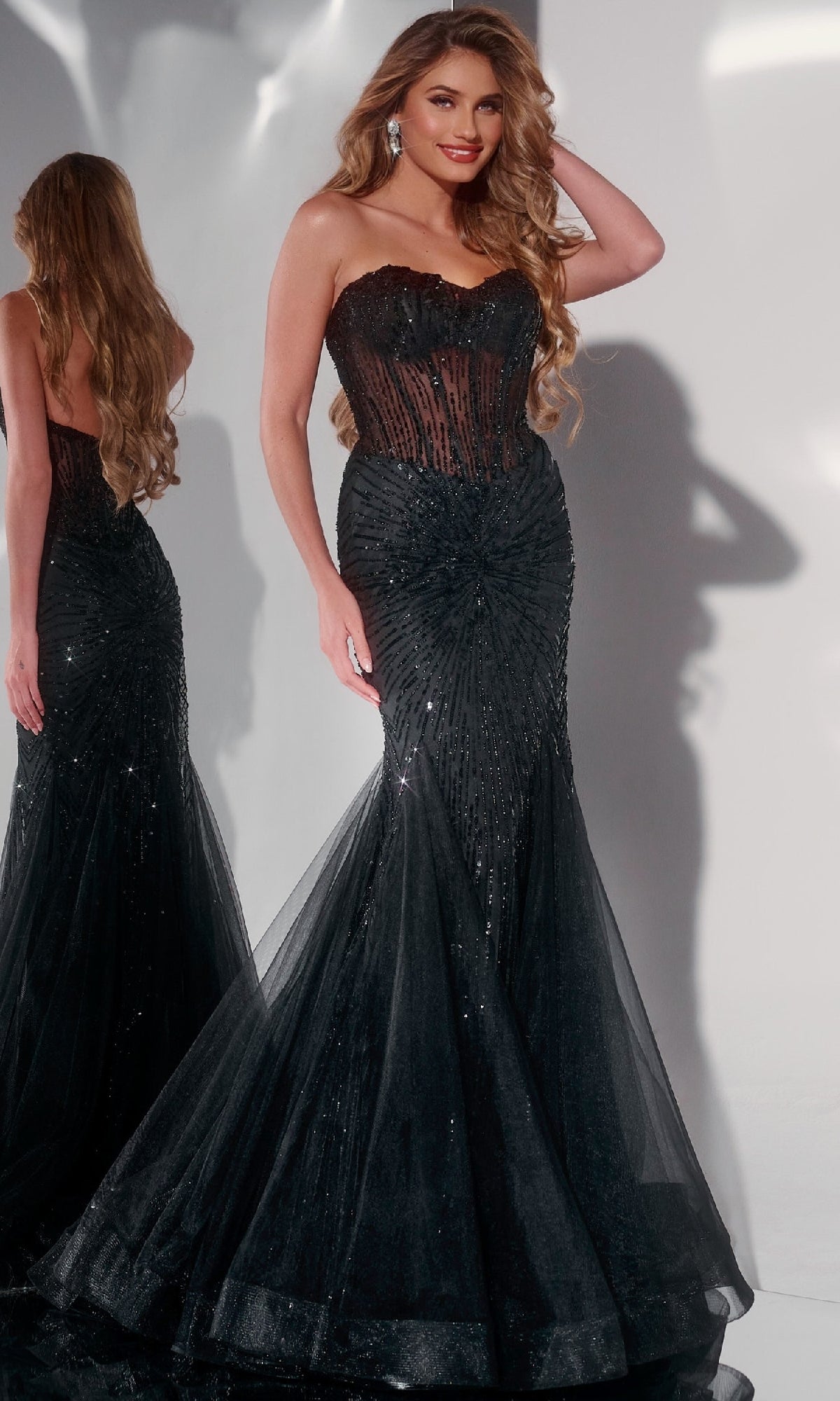 A woman poses elegantly in front of a mirror wearing the Jovani 42217 long prom dress—a strapless mermaid gown with a sheer corset bodice and dazzling sequin embellishments.